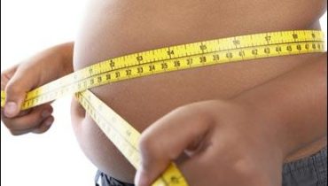 A man measures his fat belly with a measuring tape. on a gray ba