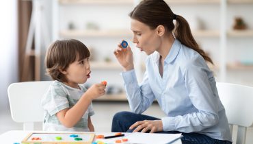 Female speech therapist curing child's problems and impediments. Little boy learning letter O with private English language tutor during lesson at office
