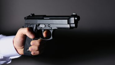 Man's hand holding gun on color background